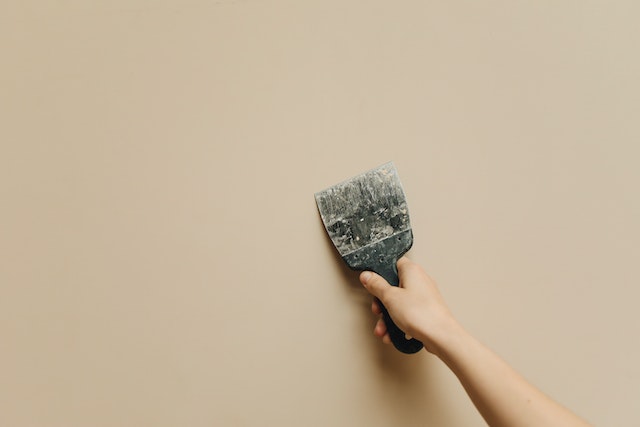 person using spackle to fix a beige wall